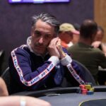 Ein Mann sitzt an einem Pokertisch und hält zwei Karten in der Hand, während er konzentriert auf seine Gegner schaut.