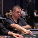 Ein Mann und eine Frau spielen Poker in einem eleganten Casino. Der Mann hält Karten in der Hand, während die Frau konzentriert auf ihre Karten schaut. Der Tisch ist mit Jetons und einem grünen Fil