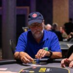 Ein Mann und eine Frau sitzen an einem Pokertisch und spielen eine Partie Poker. Der Mann hat gerade seine Karten angesehen und scheint konzentriert zu sein, während die Frau mit einem nachdenklichen Gesichtsa