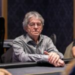Ein Mann mit einem Pokerchip in der Hand, der konzentriert in die Ferne schaut, während im Hintergrund das Casino zu sehen ist.