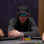 Ein Poker-Tisch mit grünem Filz, umgeben von Spielkarten, Pokerchips und Getränken. Vier Personen sitzen um den Tisch herum und spielen Poker in einer gemütlichen Atmosphäre.