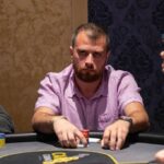 Ein Pokertisch mit grüner Filzdecke, umgeben von Spielern, die Karten halten und Pokerchips stapeln. In der Mitte des Tisches liegen Spielkarten und ein Stapel Chips.