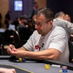 Ein grüner Pokertisch mit Spielkarten, Jetons und Getränken, umgeben von Spielern in einem Casino.