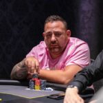 Ein Mann und eine Frau sitzen lächelnd an einem Pokertisch, während sie Karten spielen. Der Mann hält Karten in seiner Hand, während die Frau mit einem Pokerchip spielt. Die beiden haben konzentrierte