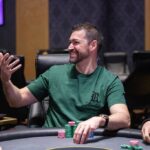 Ein Mann und eine Frau sitzen an einem Pokertisch, konzentriert auf ihre Karten und Chips. Die Frau hat eine Hand am Kinn und schaut nachdenklich, der Mann hat seine Hand am Kopf und wir