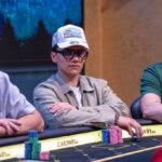 Ein professioneller Pokertisch mit grünen Filz und Spielkarten, umgeben von Pokerchips und Getränken in Gläsern. Personen sind beim Spielen zu sehen.