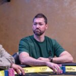 Ein Mann und eine Frau sitzen an einem Pokertisch und spielen eine Partie Poker. Der Mann hält Karten in der Hand, während die Frau konzentriert auf ihre eigenen Karten schaut. Im Hintergrund sind Poker