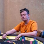 Ein Mann und eine Frau spielen Poker am Tisch in einem Casino. Der Mann hat eine Hand mit Karten in der Luft, während die Frau ihre Karten betrachtet. Das Bild zeigt eine spannende Pokerrunde in vollem G