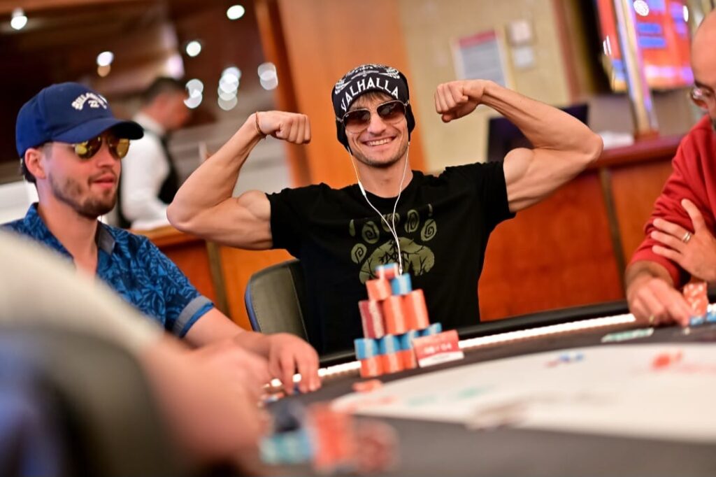 Ein Mann und eine Frau sitzen in einem Café und spielen gemeinsam Poker. Der Mann hat eine Hand mit Karten in der Luft, während die Frau auf ihre Karten schaut. Sie lächeln und scheinen Spaß zu haben.