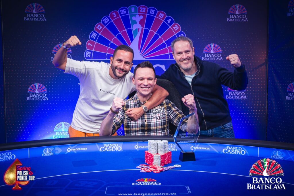 Ein Spieler mit einem breiten Lächeln hält stolz einen großen Pokal in die Luft, umgeben von jubelnden Zuschauern. Der Hintergrund zeigt eine Poker-Turnierbühne mit grellen