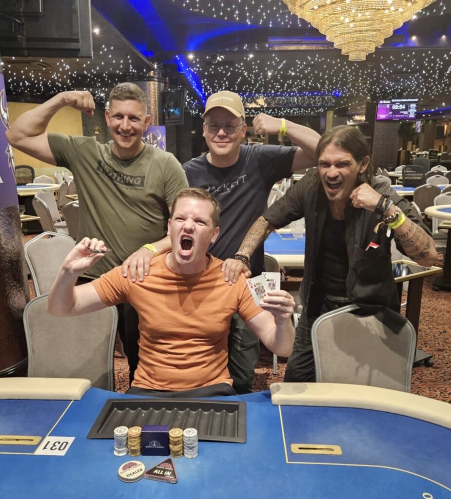 Ein Mann spielt Poker an einem eleganten Holztisch, umgeben von anderen Spielern in einem stilvollen Casino. Die Atmosphäre ist gespannt, während er seine Karten betrachtet und über seinen nächsten Zug nachden
