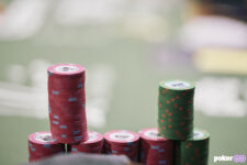 Ein Stapel von bunten Pokerchips auf einem grünen Tisch, der während der World Series of Poker platziert ist. Ein Spieler ist im Hintergrund zu sehen, der seine Karten betrachtet.