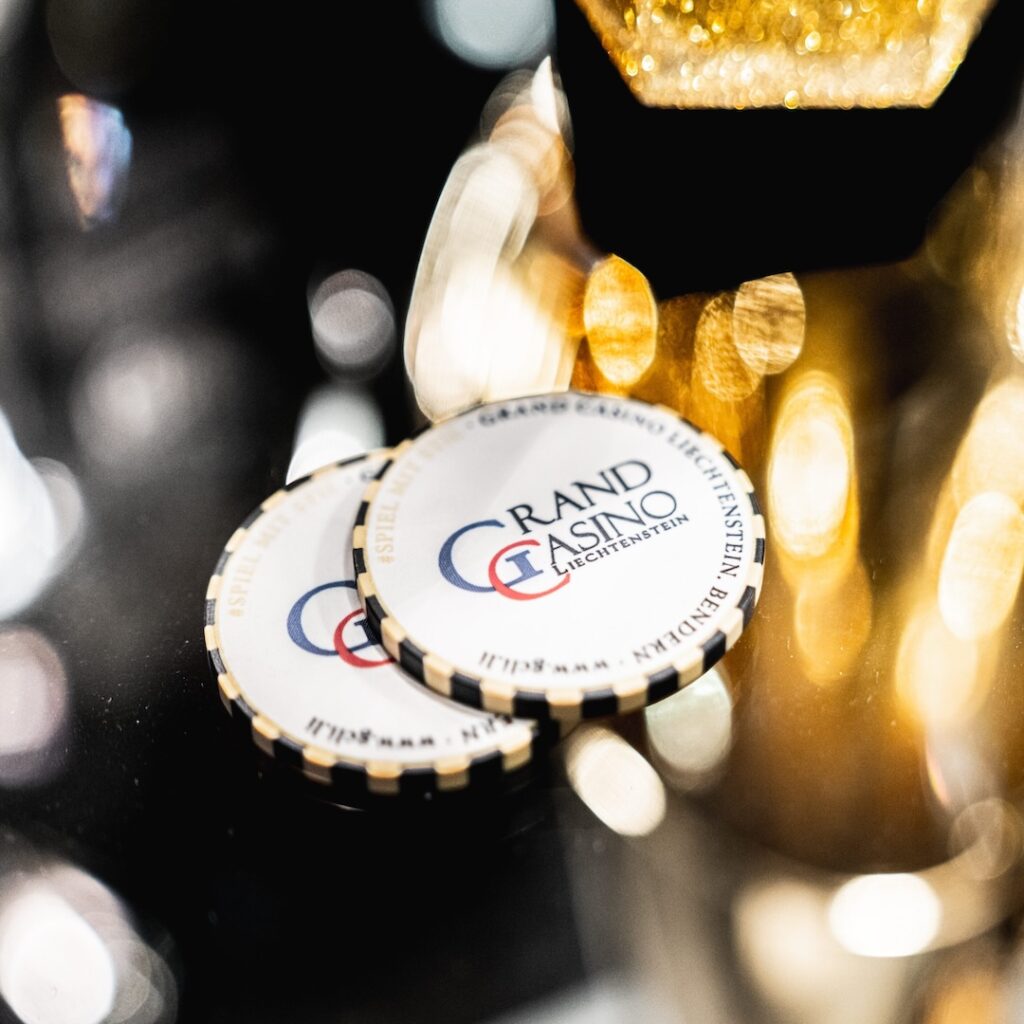 Ein Pokerturnier mit mehreren Spielern, die um einen Tisch herum sitzen und Karten halten. Einige Spieler tragen Sonnenbrillen und konzentrieren sich auf ihre Hände. Der Dealer in der Mit