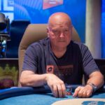 Ein Mann sitzt an einem Pokertisch während eines Turniers im King's Resort in Rozvadov. Er konzentriert sich auf seine Karten, umgeben von anderen Spielern und Dealer.