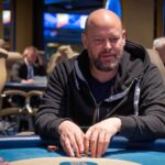 Ein Mann sitzt an einem Pokertisch mit grüner Filzdecke während eines Pokerturniers im King's Casino in Rozvadov. Er trägt eine Sonnenbrille und hat Pokerchips vor sich auf dem T