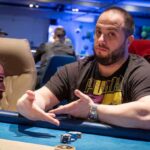 Ein Mann sitzt an einem Pokertisch während eines Pokerturniers im Rahmen des "The Festival Rozvadov Mixed Games Main Event". Er trägt ein dunkles Hemd und eine Mütze und betrachtet konzentriert