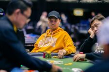 Ein Mann sitzt an einem Pokertisch während eines Turniers der World Series of Poker. Er trägt eine Sonnenbrille und konzentriert sich auf seine Karten. Andere Spieler und Zuschauer sind im Hintergrund