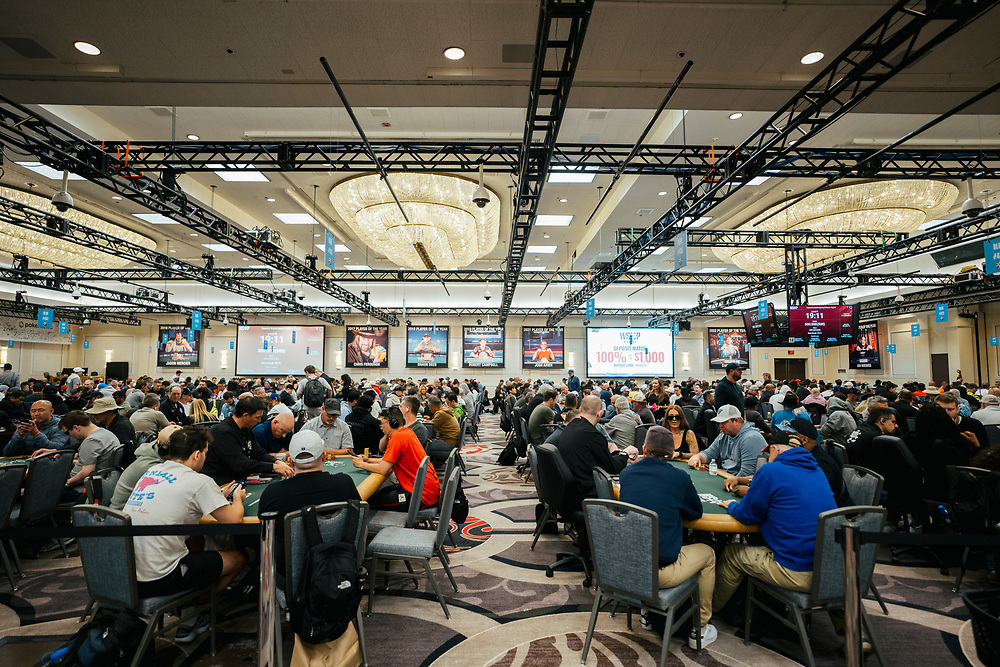 Ein professioneller Pokerspieler mit Sonnenbrille und Kappe sitzt an einem Tisch während der World Series of Poker (WSOP) und betrachtet konzentriert seine Karten.