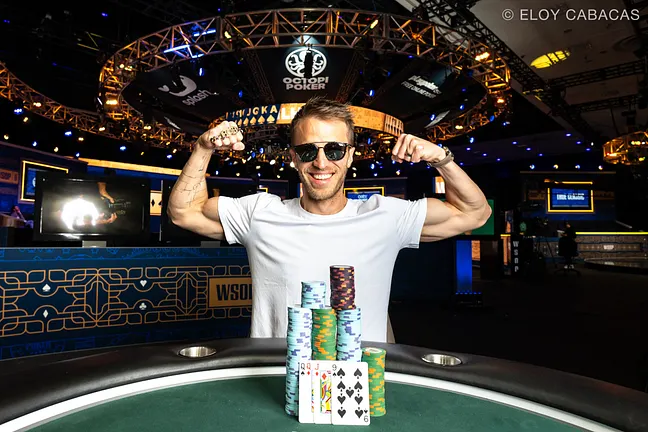 Ein professioneller Pokertisch mit grünem Filz, umgeben von Spielkarten, Pokerchips und Getränken in Gläsern. Vier Personen sitzen um den Tisch herum und halten ihre Karten